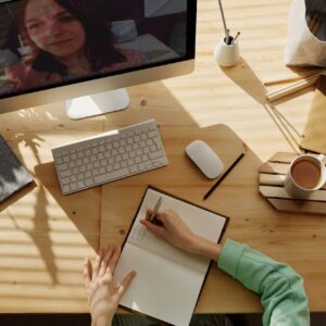 A student taking notes during a video call for online learning at home.